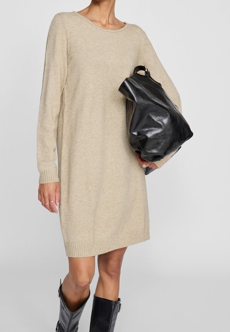 Abito in maglia beige con maniche lunghe, polsini a costine e orlo. Abbinato a una borsa a tracolla in pelle nera e stivali neri al ginocchio.