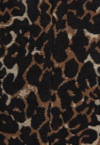 Tejido de estampado de leopardo con una superficie texturizada, que presenta patrones audaces en negro y marrón sobre un fondo beige claro.