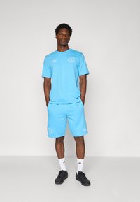 Light blue athletic outfit consisting of a short-sleeve t-shirt and shorts, with embroidered logos. Pair of black athletic shoes and white socks.