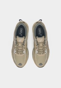 Ζευγάρι μπεζ και γκρι αθλητικά παπούτσια Asics με κορδόνια, από πάνω, σε απλό λευκό φόντο.