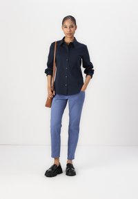 Navy button-up shirt with long sleeves, paired with light blue fitted pants. Black chunky loafers and a brown shoulder bag complete the look.