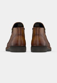 Brązowe skórzane botki do kostki o zaokrąglonym kształcie, z bocznymi zamkami błyskawicznymi, kontrastującymi ciemnymi podeszwami i minimalnymi detalami przeszyć.