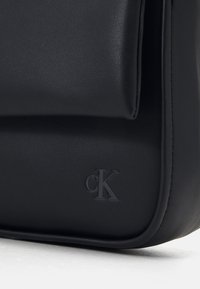 Borsa a spalla in pelle nera con texture liscia, caratterizzata da un logo impresso discreto e un design minimalista. Bordo arrotondato e senza hardware visibile.