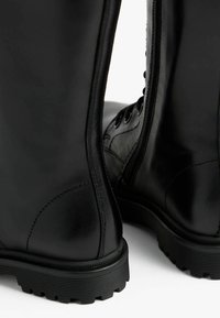 Black leather ankle boots with smooth texture, lace-up front, and side zipper. Treaded rubber sole offers grip and durability.