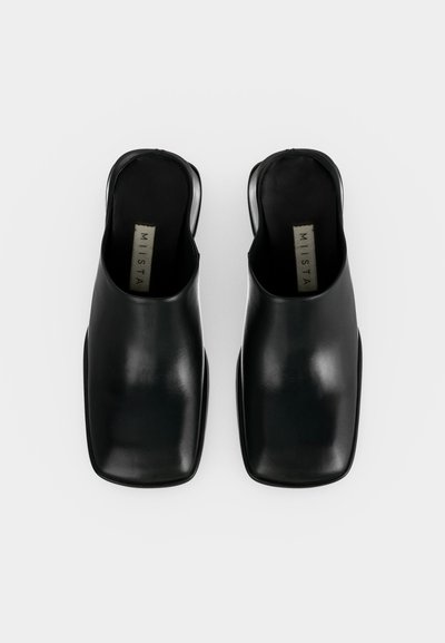 Ζευγάρι μαύρα δερμάτινα παπούτσια χωρίς κορδόνια με τετράγωνες μύτες και ανοιχτές φτέρνες, σε θέα από πάνω σε λευκό φόντο.