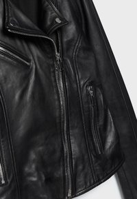 Schwarze Lederjacke mit silbernen Reißverschlüssen an den vorderen Taschen und asymmetrischem Reißverschlussverschluss auf einer schlichten Hintergrund.