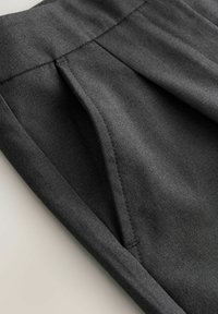 Graue Stoffhose mit Falten, seitlicher Tasche und glatter Textur. Der Bund ist sauber mit Nähten verarbeitet.
