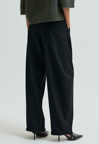 Široké čierne nohavice s hladkou textúrou, s dvoma zadnými vreckami a pohodlným strihom, ktoré sú skombinované s čiernymi lodičkami s špicatou špičkou.