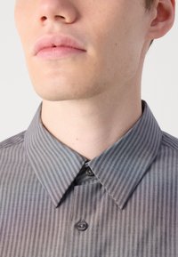 Camisa de botón a rayas grises con cuello clásico, que presenta una textura suave y un solo botón en el cuello. Los patrones son sutiles y lineales.