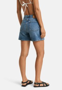 Lichte blauwe denim shorts, met een hoge taille, achterzakken en een rechte pijp. Gepaard met zwarte sandalen met bandjes.