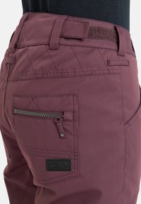 Bordeaux ski-broek met een gestructureerd oppervlak, verstevigde riemlussen, een zijzak met ritssluiting en een zwart logo-label. Met een gewatteerd ontwerp.