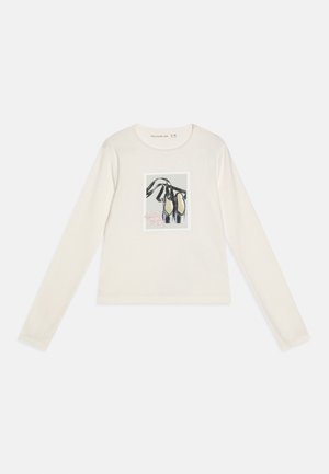 Cămașă pentru copii cu mânecă lungă, crem, cu imprimeu cu pantofi de balet și panglici negre în partea din față, în centru.