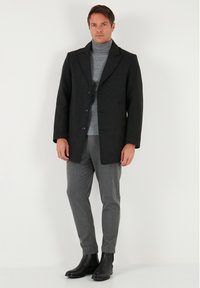 Tume villane mantlid, millel on sälkkraed ja kolm nuppu, kombineeritud halli kõrge kaelusega kampsuniga. Komplekti kuuluvad hallid kitsad püksid ja mustad pahkluu saapad.