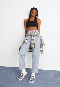 Black sports bra, light blue trousers, and black-and-white checkerboard slip-on shoes. A plaid shirt tied around the waist.