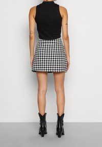 Haut noir sans manches associé à une jupe courte à motif pied-de-poule noir et blanc. La tenue est complétée par des bottines à talons noires.