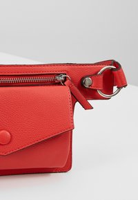 Borsa in pelle rossa con finitura testurizzata, dotata di un comparto principale con zip, chiusura a scatto e una tracolla regolabile con dettagli metallici.