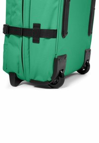 Zelený skládací kufr s texturovanou tkaninou, černými komponenty, nastavitelným popruhem a pevnými koly pro snadnou mobilitu. Kompaktní tvar a designové detaily.