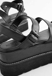 Sandales à plateforme noires avec des sangles en cuir lisses, des boucles réglables, une semelle en daim texturé et un détail de couture blanche contrastante.