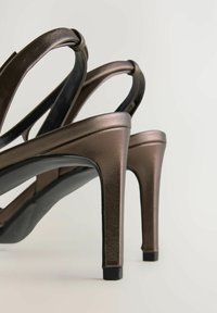Sandali con tacco alto dal finish bronzo lucido, caratterizzati da un design elegante e cinturini sottili, posizionati su uno sfondo chiaro.