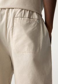 Shorts en coton beige avec une ceinture élastique, dotés d'une seule poche arrière cousue avec un fil assorti et d'une petite étiquette sur la poche.