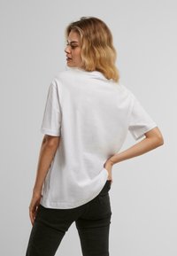 Tricou alb din bumbac, cu m�âneci scurte, decolteu rotund și o croială lejeră. Prezintă un tiv ușor curbat în partea din spate.