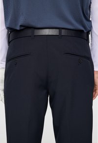 Marineblauwe golfbroek van soepel materiaal, met een slim fit, achterzakken met knopen en een zwarte leren riem.