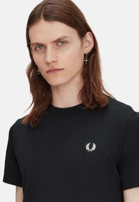 Camiseta de algodón negra con un logo bordado blanco en el lado izquierdo del pecho, mangas cortas y un cuello redondo clásico.