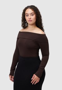 Brązowa bluzka z długim rękawem i odsłoniętymi ramionami, wykonana z gładkiego materiału, zestawiona z dopasowaną czarną spódnicą. Minimalistyczny design bez wzorów.