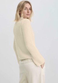 Cremfarbener, gerippter Pullover mit langen Ärmeln und rundem Ausschnitt, der ein strukturiertes Strickmuster und eine lockere Passform aufweist.