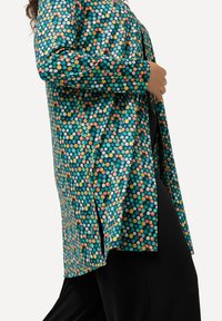 Camicia lunga con una base turchese ricoperta di pois multicolore. Presenta maniche lunghe e fessure laterali per agevolare i movimenti.
