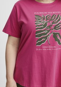 Magentové bavlněné tričko s velkým zeleným listem a bílým textem. Design obsahuje jak tištěný text, tak i detaily listu.