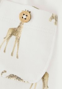 Tissu blanc avec imprimé girafe dorée. Un bouton rond en bois avec une découpe en forme de fleur sécurise une poche en haut. Texture lisse et détails délicats.