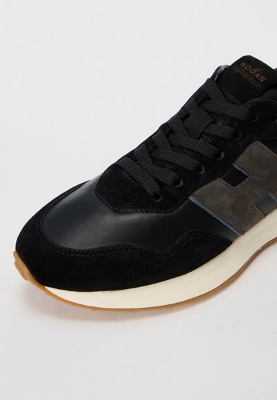 Mustad ja hallid Hogan tennisekingad nahast ja suede paneelidega, mustade paeltega ja valge vahega kerge tausta peal.