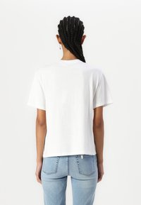 T-shirt bianca in cotone a maniche corte, colletto a giro, e orlo dritto, mostrata di schiena con jeans in denim azzurro.