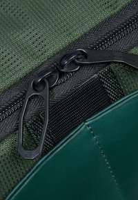 Primo piano di due cursori di zip neri su tessuto verde testurizzato e pannello cucito in pelle verde scuro liscia.