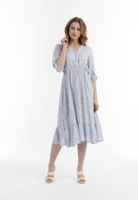 Rochie florală de culoare albastru deschis pastel, până la genunchi, cu un sistem de închidere cu butoni în față, talie elastică și maneci bufante cu trei sferturi. Prezintă un tiv evazat.