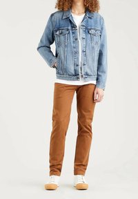 Jeansjacka i ljusblått, design med knappar framtill och två bröstfickor. Kombinerad med bruna tapered-byxor och vita sneakers.