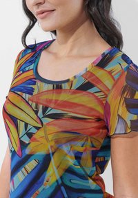 Buntes T-Shirt mit kurzen Ärmeln, das ein lebhaftes tropisches Blattmuster in Orange-, Blau- und Gelbtönen zeigt, mit einem Rundhalsausschnitt.