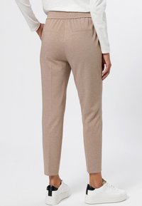 Beige, slim-fit trousers with an elastic waistband and back pockets, featuring a smooth texture, paired with white sneakers with black accents.