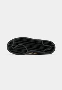 Black rubber sneaker sole with herringbone pattern, featuring gold accents and a smooth edge, designed for grip and flexibility.