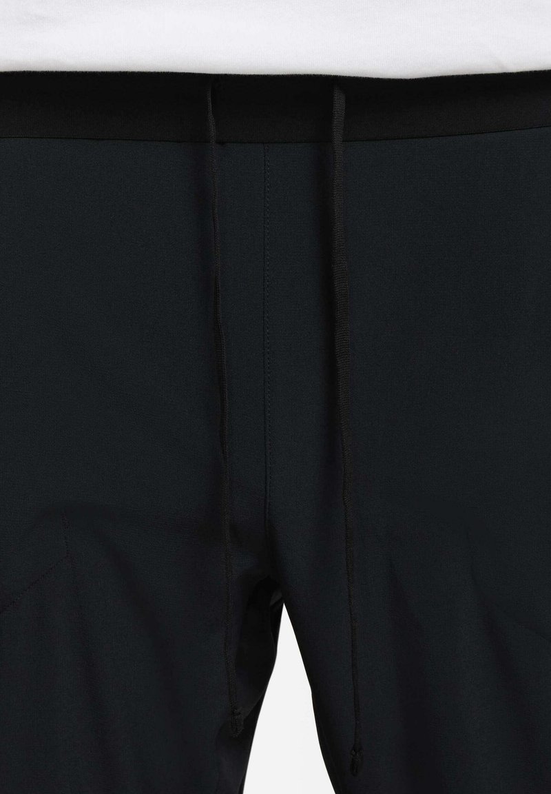 Shorts de sport noirs avec une texture lisse, présentant une taille noire et des cordons de serrage ajustables. Des poches latérales sont visibles.