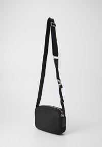 Borsa a tracolla nera con forma rettangolare, materiale in tessuto, chiusura con zip, tracolla regolabile e dettagli in metallo.