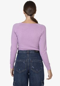 Maglione lungo a maniche, di colore viola chiaro, con scollo rotondo, abbinato a un pantalone in denim scuro a vita alta con tasche applicate e un aspetto vissuto.