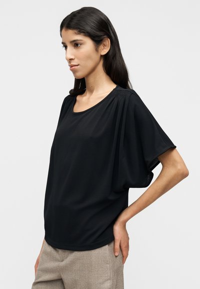 Μαύρο κοντομάνικο τοπ με στρογγυλή λαιμόκοψη, διαθέτει ντραπέ ύφασμα, ομαλή υφή και διακριτικό σούρωμα στους ώμους.