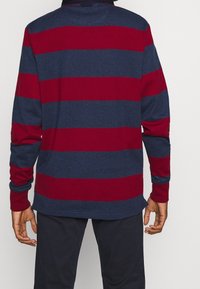 Langarm-Poloshirt in navy und bordeaux gestreift, aus weichem Stoff gefertigt. Verfügt über einen umschlagbaren Kragen und gerippte Bündchen.