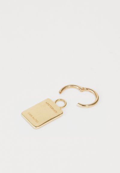 Breloc din metal auriu, cu un tag rectangular pe care este gravat un text și un inel circular de atașare. Suprafață netedă și lucioasă, cu un design minimalist.