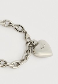Ασημένια αλυσίδα βραχιόλι με μεγάλους οβάλ συνδέσμους και γυαλιστερό charm σε σχήμα καρδιάς, με χαραγμένα τα αρχικά σε λευκό φόντο.