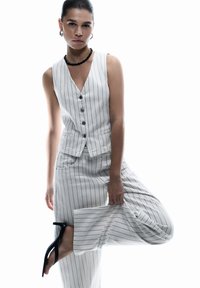 Gestreept twee-delig outfit met een mouwloze vest met knopen en wijde broekspijpen. Gemaakt van een lichtgewicht stof in wit en grijs.