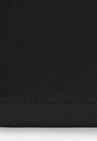 Gros plan d’un tissu noir montrant une couture double horizontale près du bord inférieur sur une surface textile lisse.