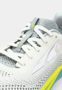 Baskets de sport blanches en maille avec des accents gris et une semelle extérieure jaune. Présente un design léger, un système de laçage proéminent et un logo détaillé.